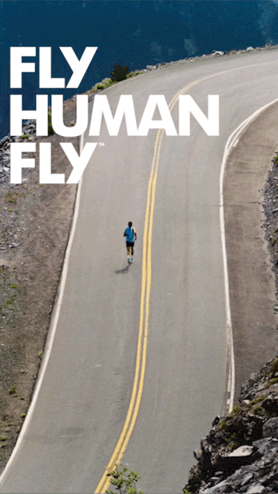 A person running alone on a winding mountain road with the text 'Fly Human Fly' overlaid. HOKA. Ariel. Running. Runner Road. Athlete.