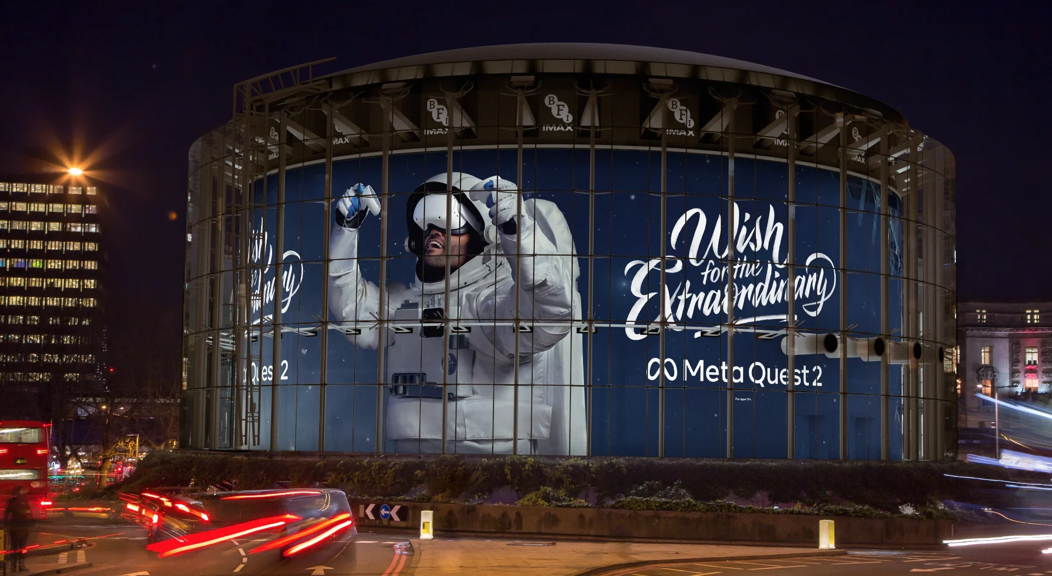 Large illuminated billboard on a building featuring an astronaut in a spacesuit adjusting his helmet, with the words "Wish for an Extraterrestrial" and logos for Meta Quest 2 virtual reality headset.