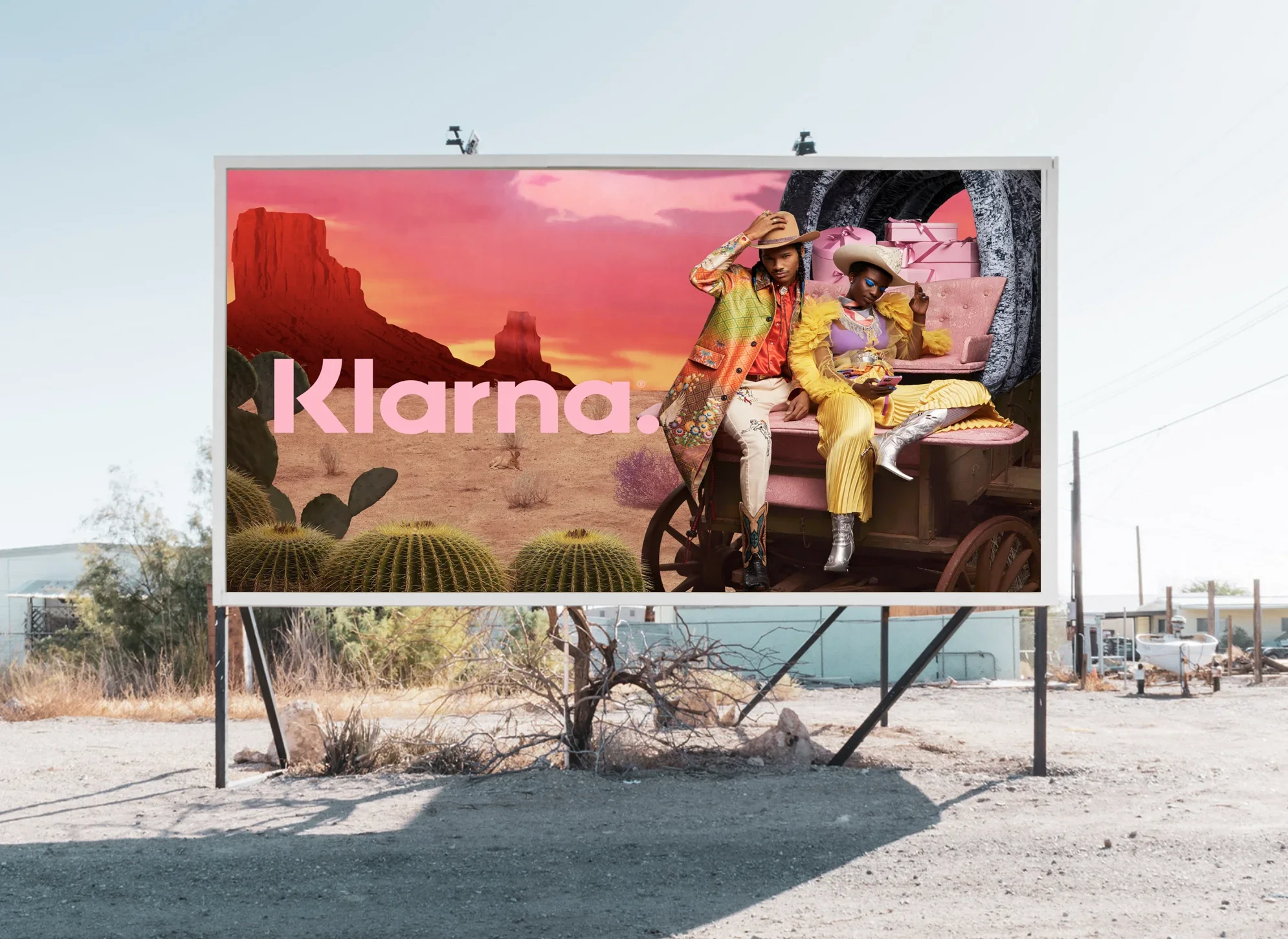 Klarna Billboard advertisement featuring two models dressed in colorful Country clothing, sitting inside a pink carriage with a desert landscape and red rock formations in the background. Advertising. Producer. Miranda Kendrick.