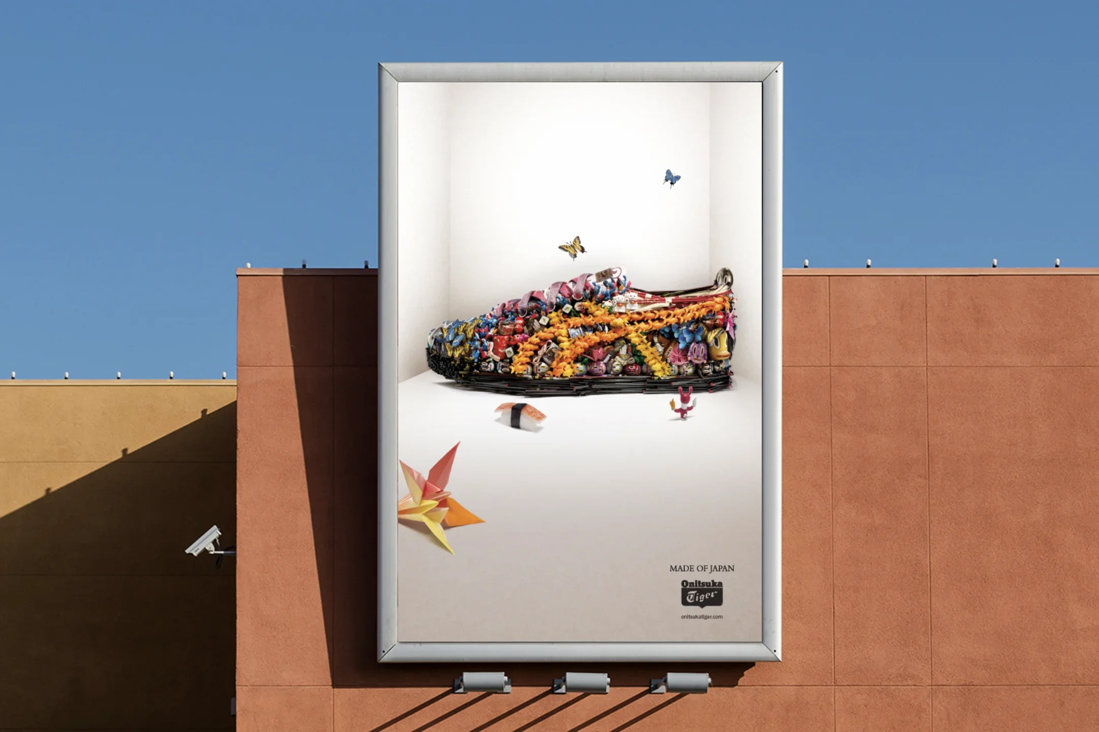 Billboard advertisement featuring a colorful origami paper crane and star, decorative elements resembling flowers and butterflies, with text indicating it is made in Japan by Onitsuka Tiger.