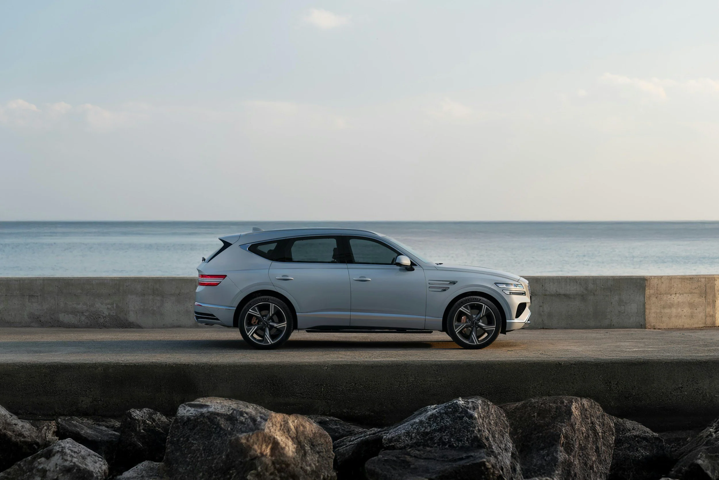 Silver SUV parked along a coastal road with rocks in foreground and ocean in background.