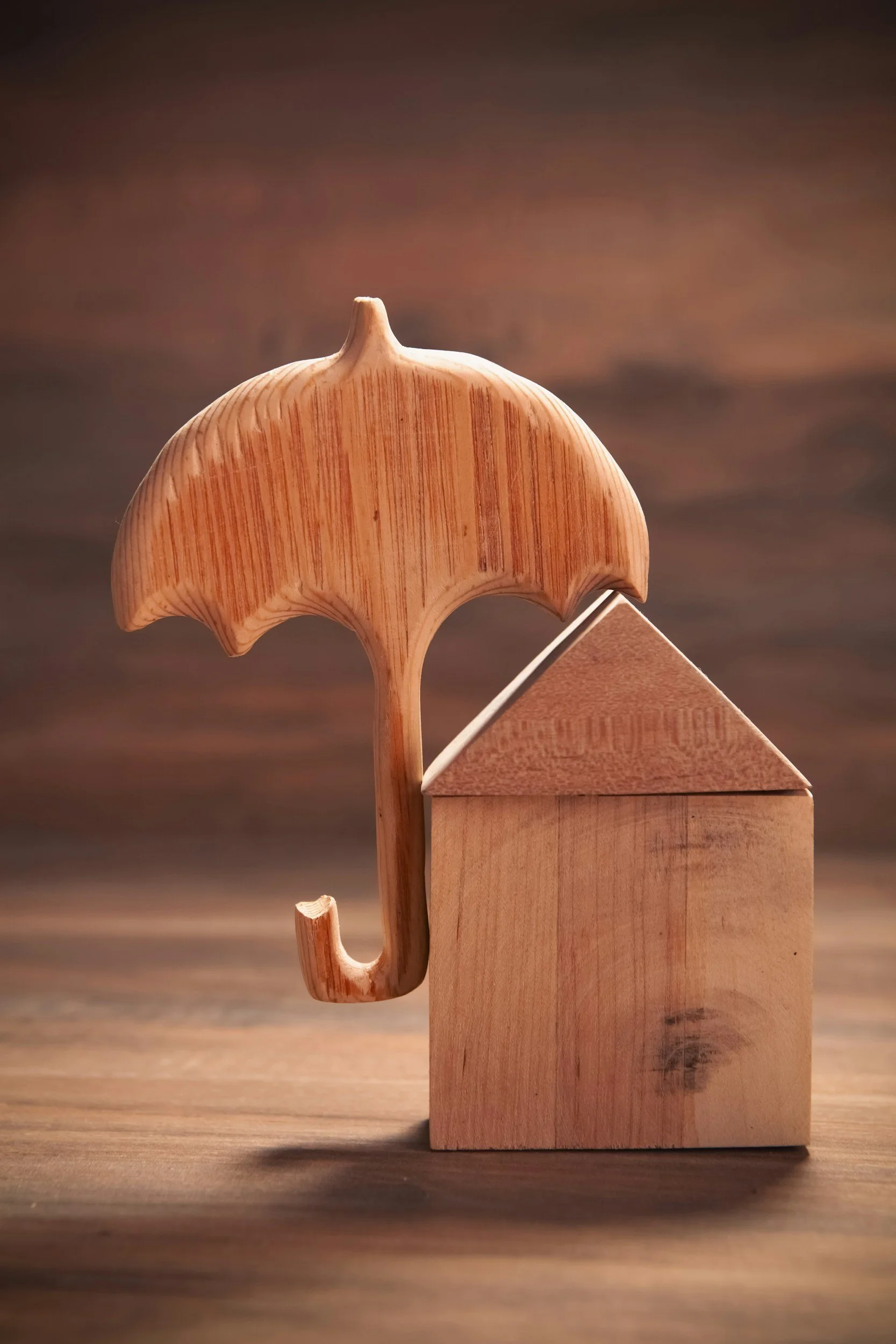 Wooden house with a roof and a large umbrella with a curved handle, all made of wood, on a wooden surface.
