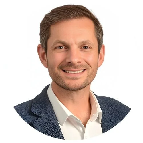 Headshot of a man with short brown hair, beard, and a smile, wearing a dark blazer and white shirt.