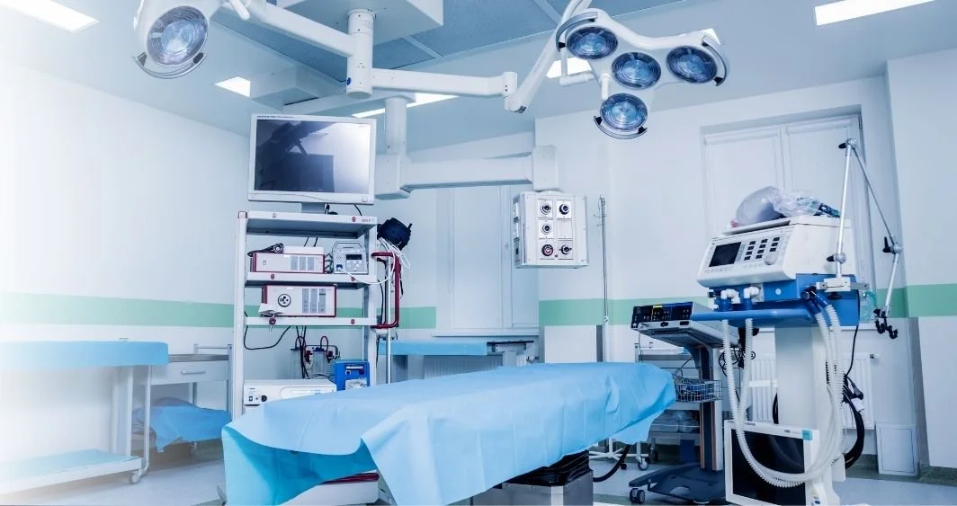 Empty hospital operating room with surgical equipment, patient bed, overhead lights, and monitoring devices.