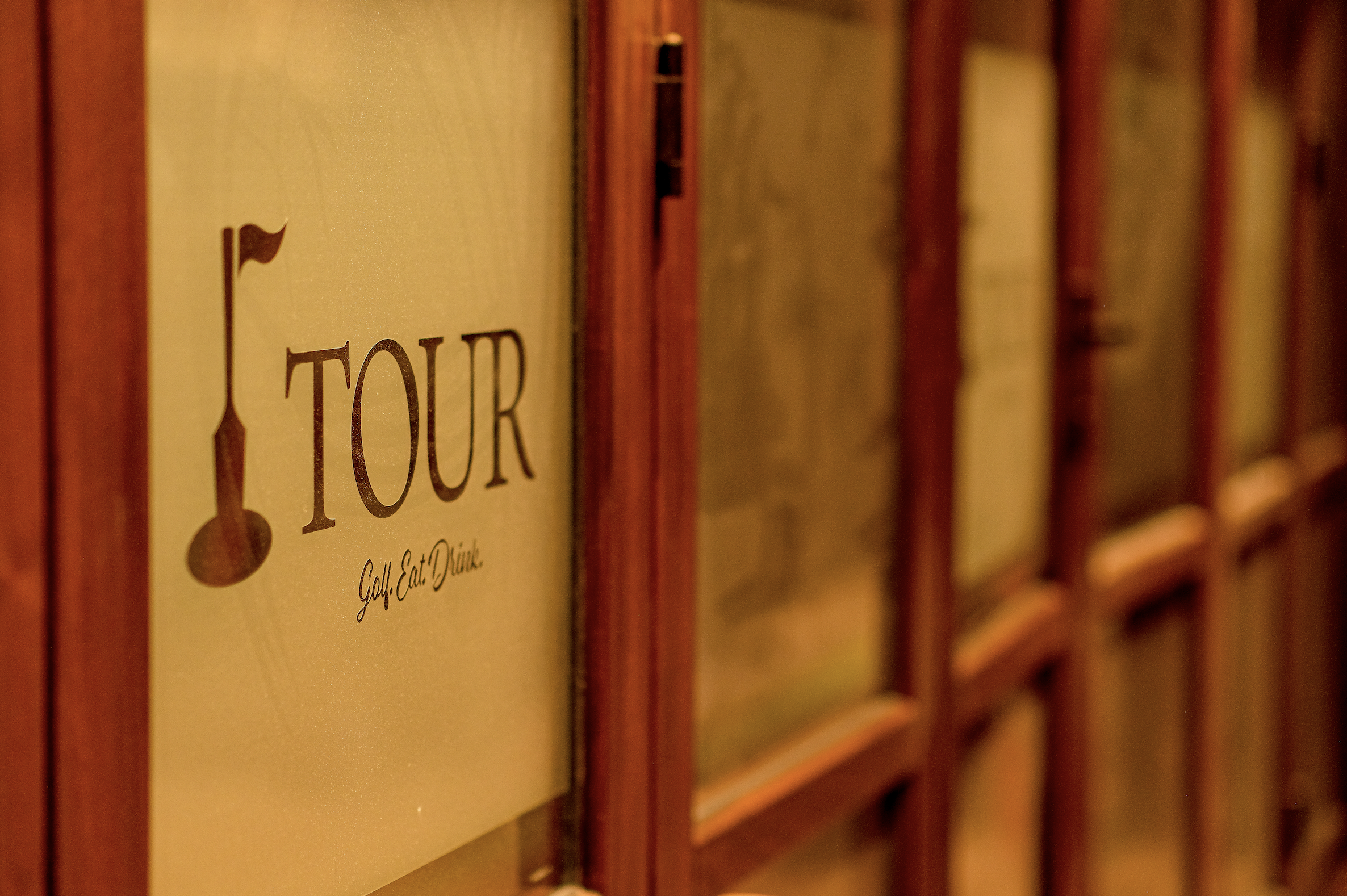 A row of books on a shelf, with the closest book titled 'TOUR' with a wine glass icon and the phrase 'Golf. Eat. Drink.' visible on the cover.