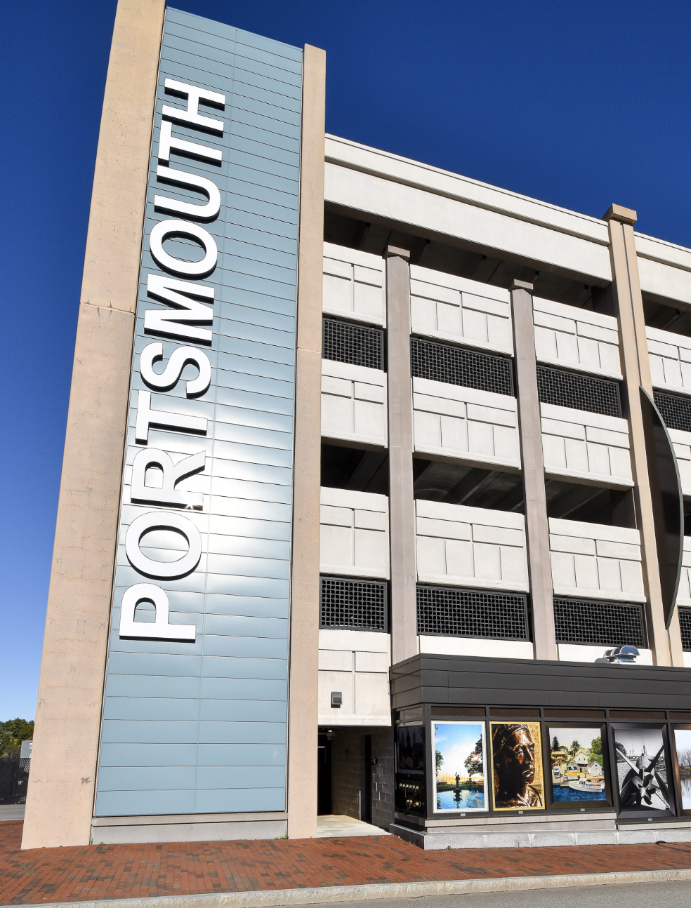 Exterior of a parking garage with a large sign reading 'PARKING LOT' on the side, and framed photographs displayed near the entrance.