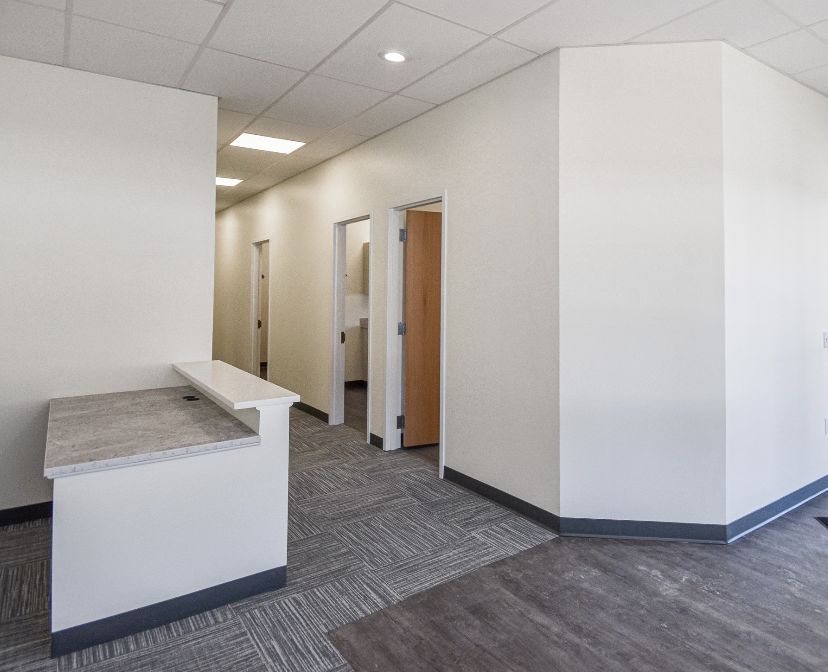 An empty hallway in an office building with multiple doors, a reception counter, and tiled flooring.