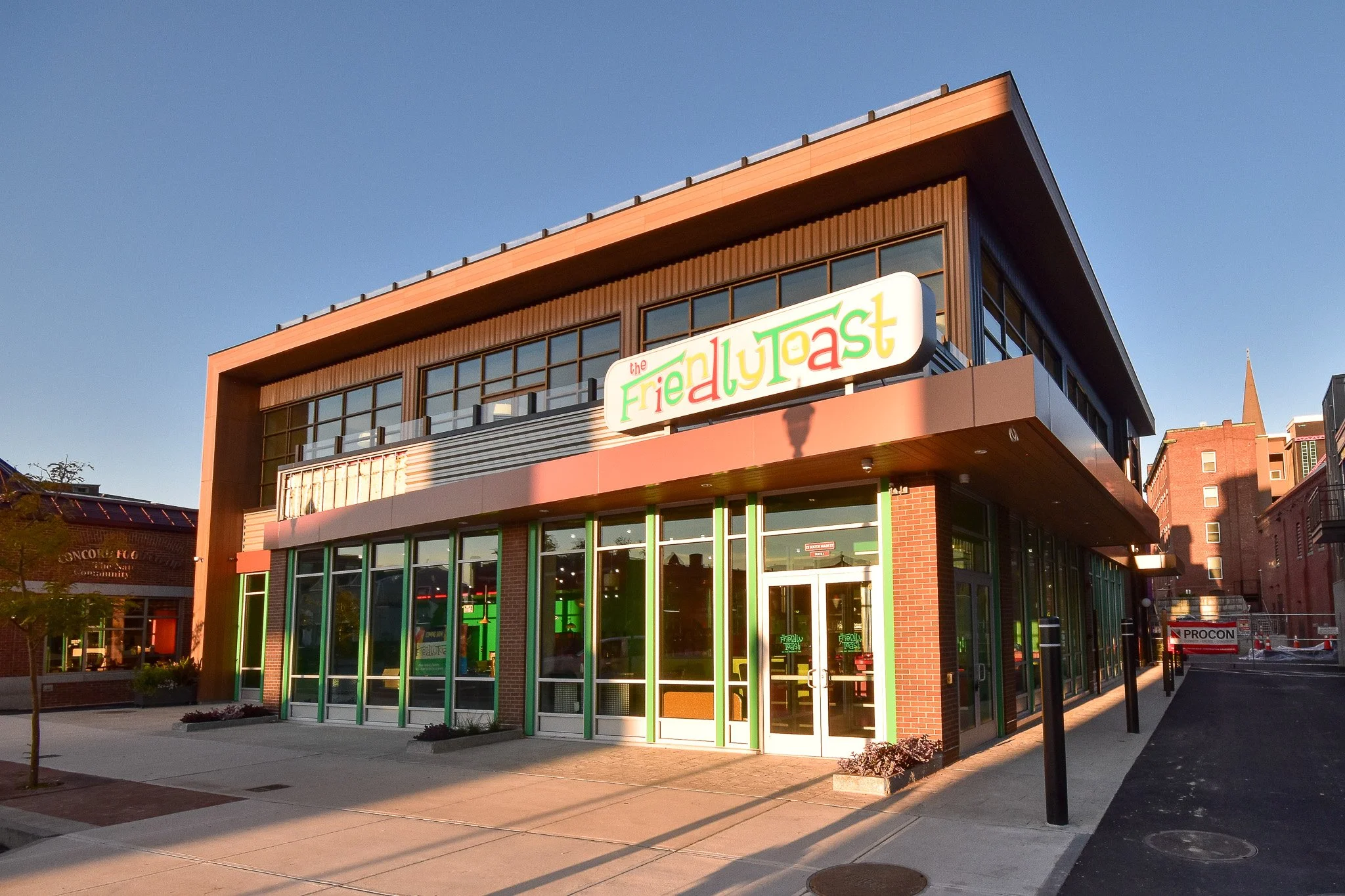 Exterior of a modern building with a sign that reads 'the FriedYogast', large glass windows, and a brick structure, with a clear blue sky overhead.