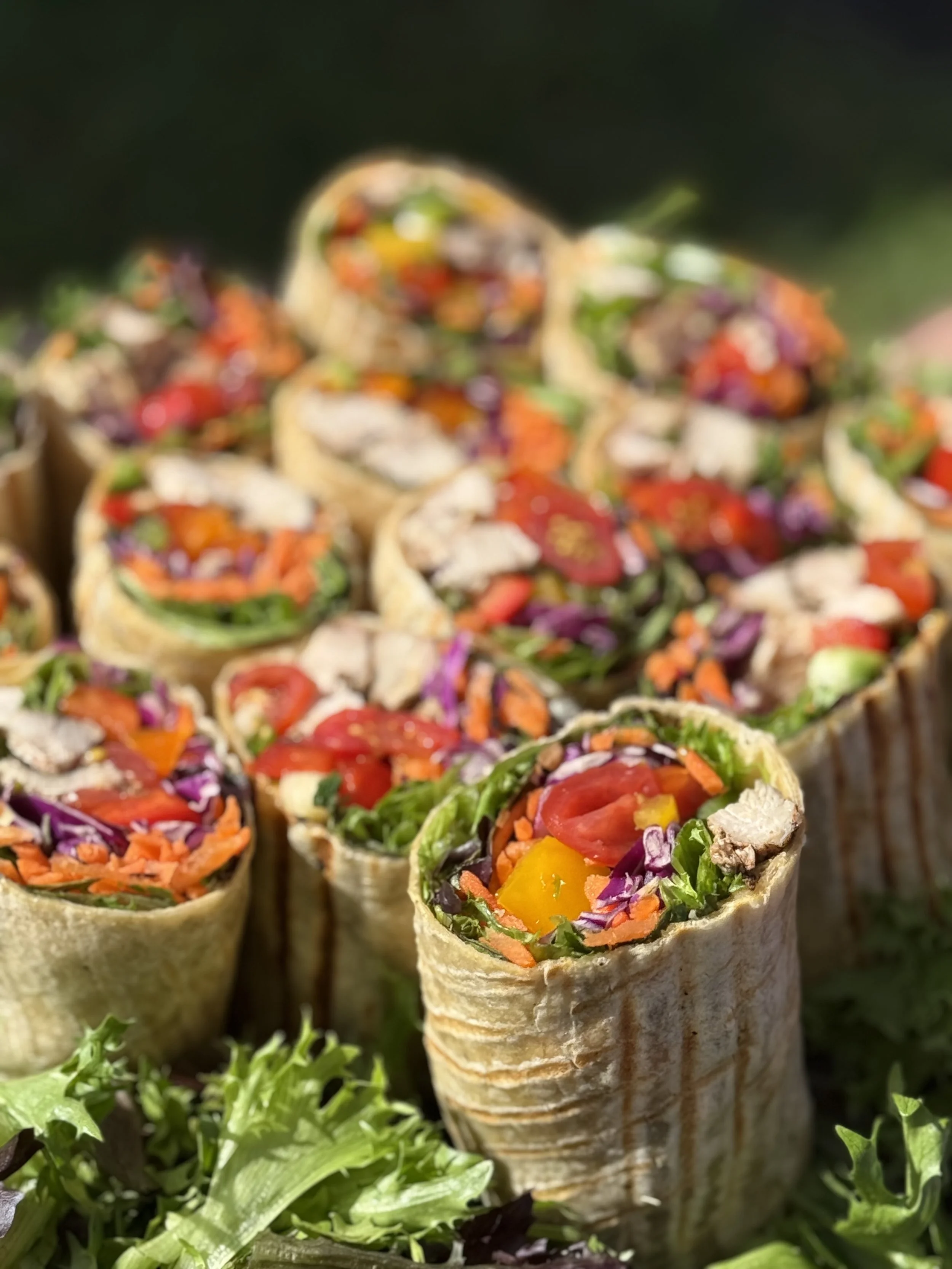 Close-up of vegetable and meat-filled wraps with colorful shredded vegetables inside a crispy shell, placed on a bed of mixed greens.