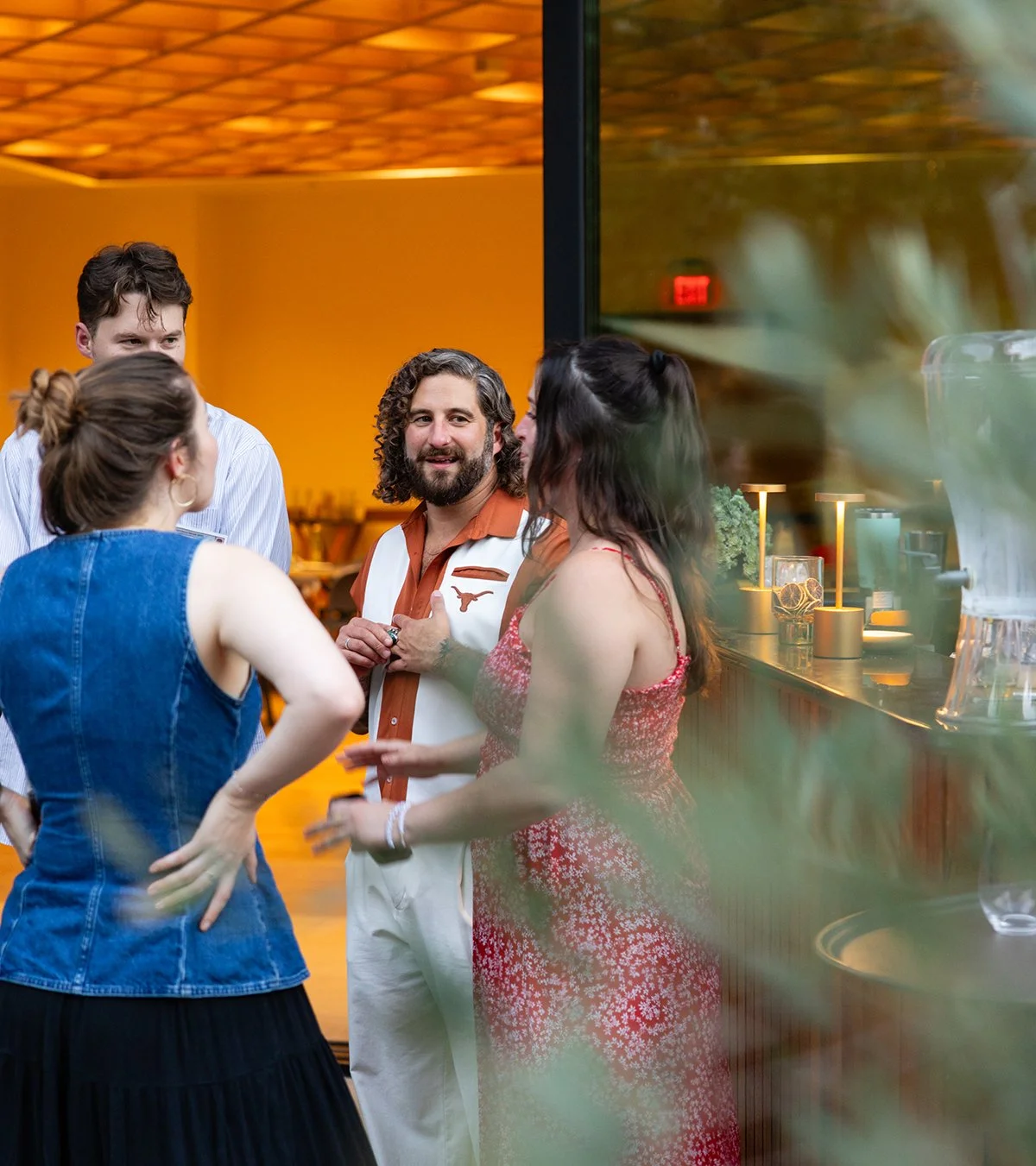 Group of five people having a conversation inside a restaurant or bar with warm lighting and a modern interior.