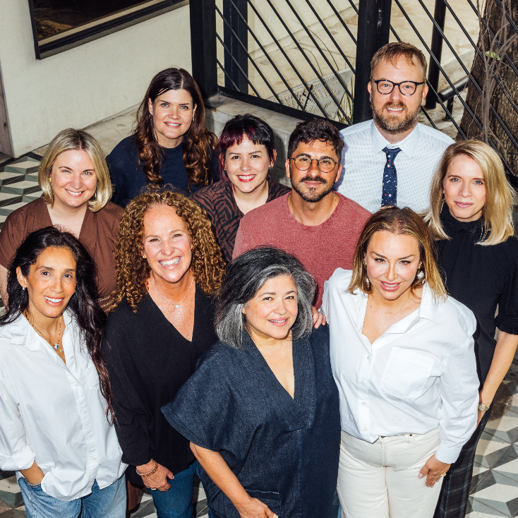 Group of ten diverse adults smiling outdoors on a staircase with a black metal railing.