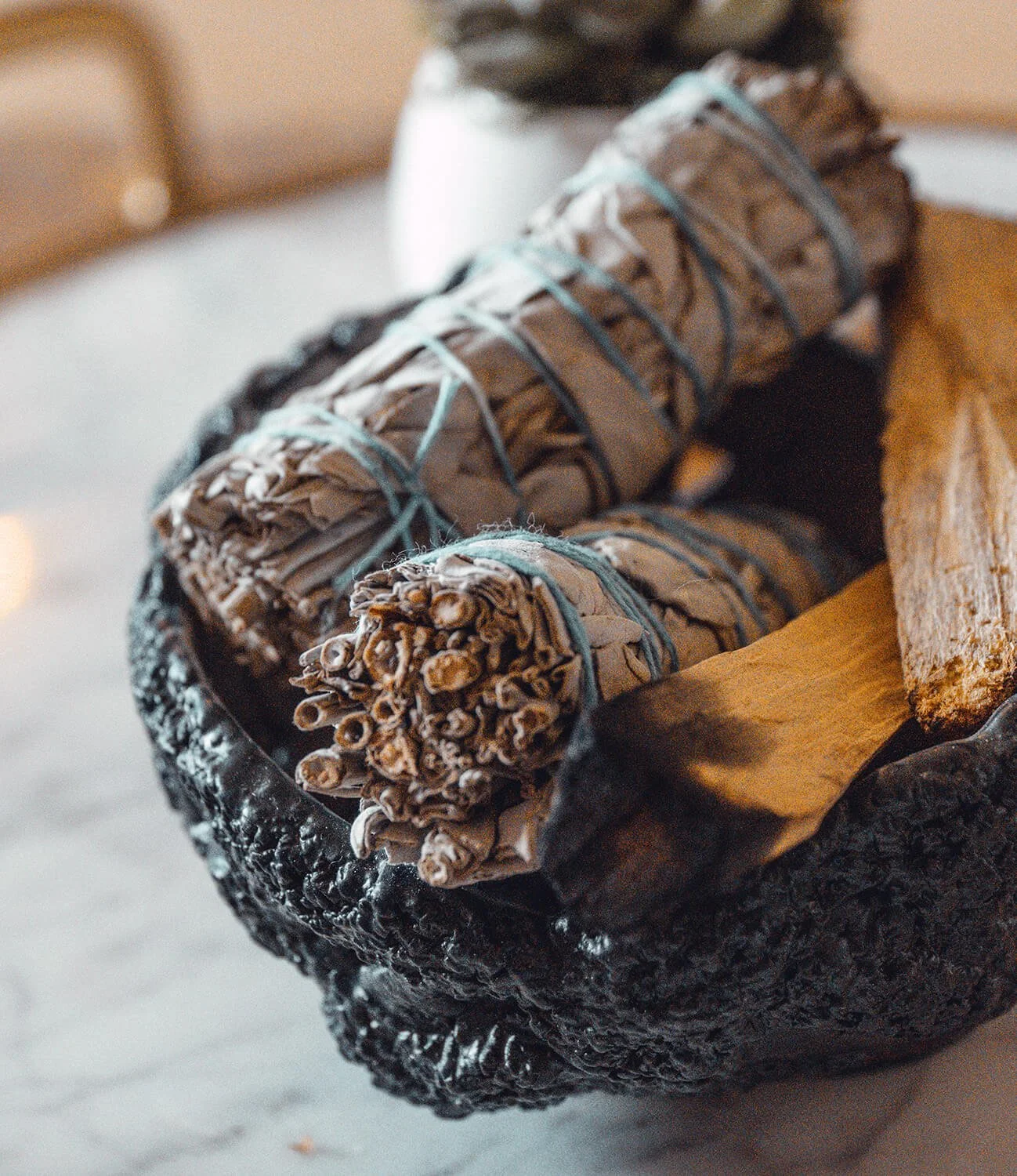 Three bundles of dried sage tied with blue string are placed on a wooden tray.