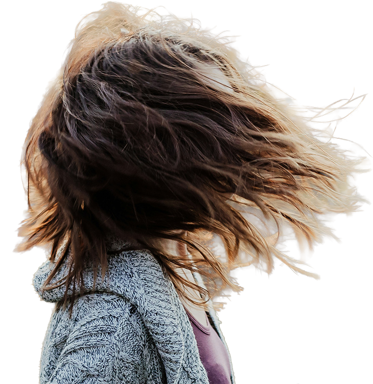 A person with long, brown hair blowing in the wind and hiding her face, wearing a textured grey coat and purple top.