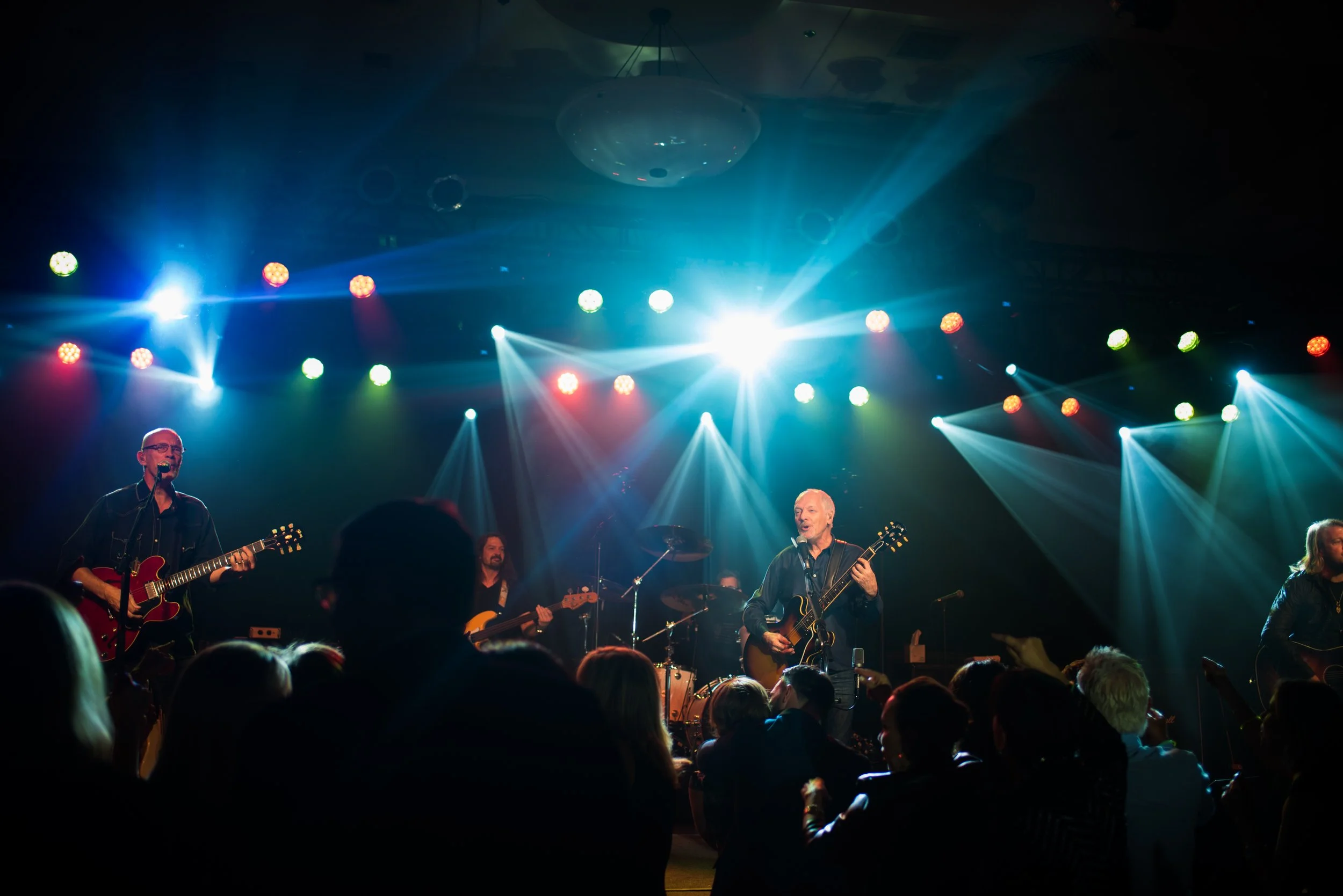 A band performing live on stage with colorful stage lighting and an audience watching.