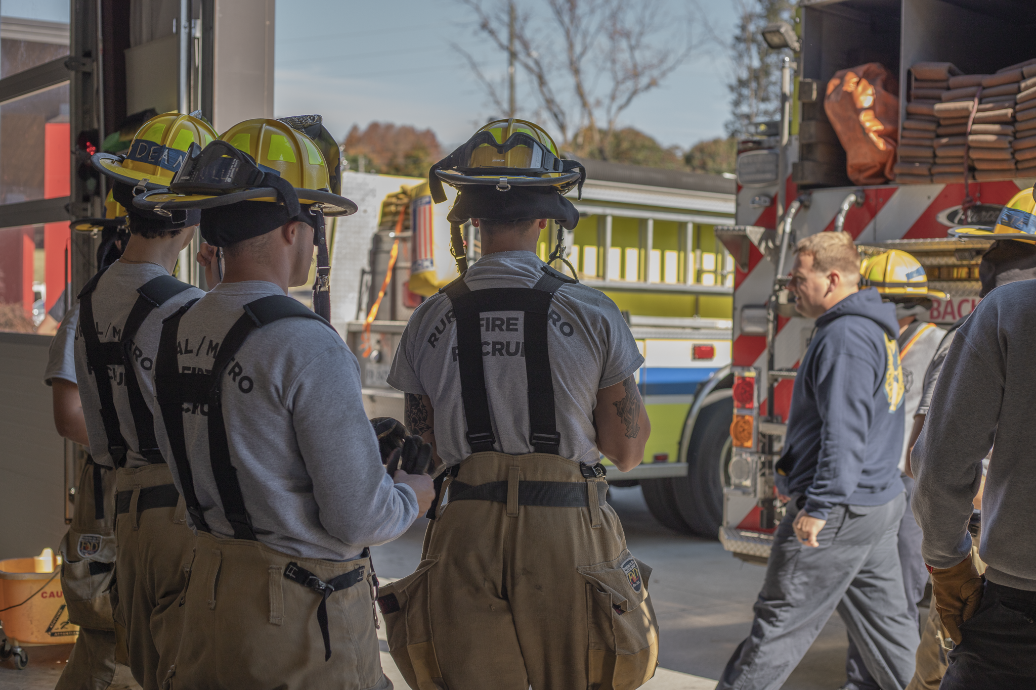 Group of firefighters wearing yellow helmets and gear standing near a fire truck, preparing for emergency response.