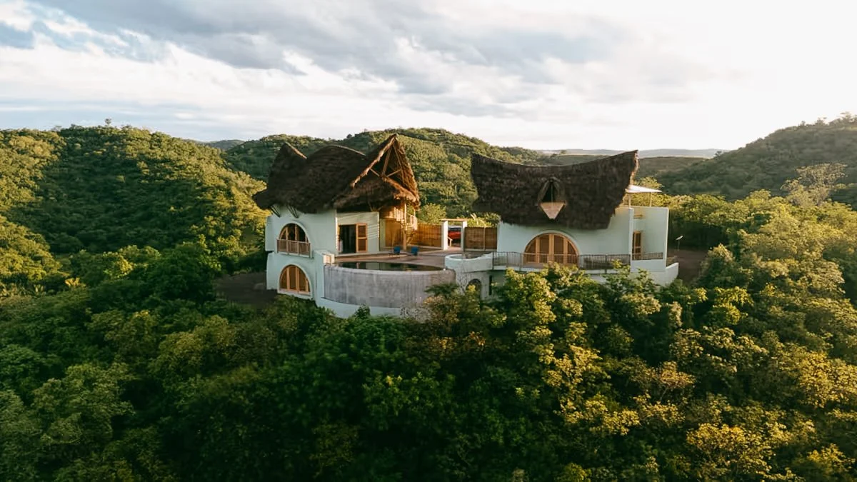 Villa Tortuga; A house with a white exterior and thatched roof, surrounded by lush green trees and hills.