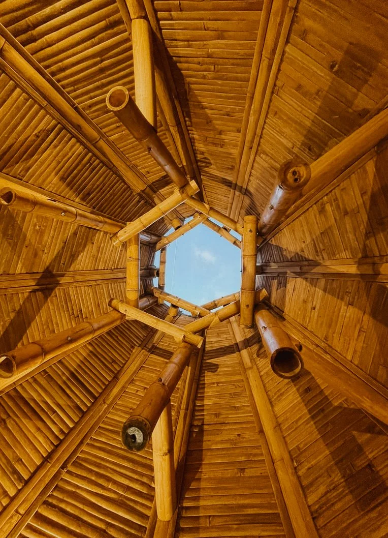 View looking up inside a bamboo hut with a hexagonal opening at the top showing the sky.