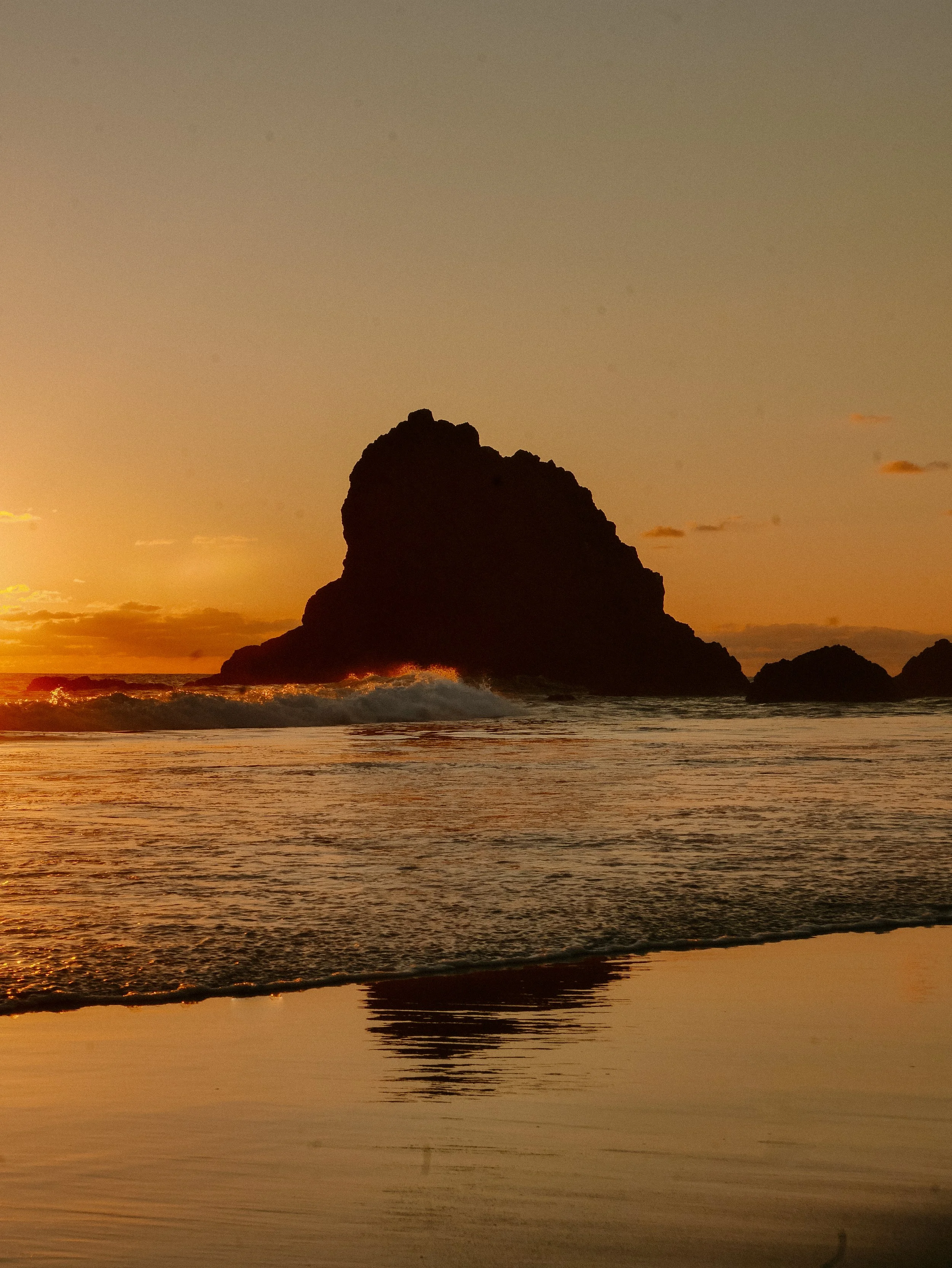 Sunset over ocean with large rocky island and reflections in the wet sand in Arroyo Seco.