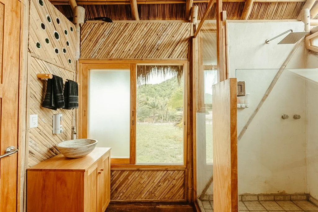 Beachfront housing; A rustic bathroom with wooden paneling, a vessel sink on a wooden vanity, and a frosted window overlooking a natural landscape with trees.