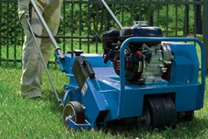 Mow right does Aeration and Dethatching. Person operating a blue turf aerator and dethatcher on a grassy area near a fence