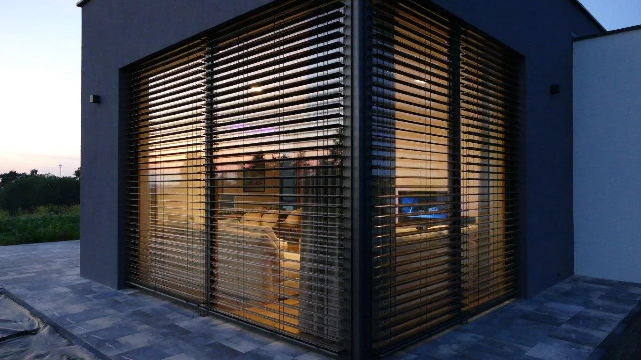 Ein modernes Haus mit großen Fenstern und horizontalen Jalousien bei Sonnenuntergang.