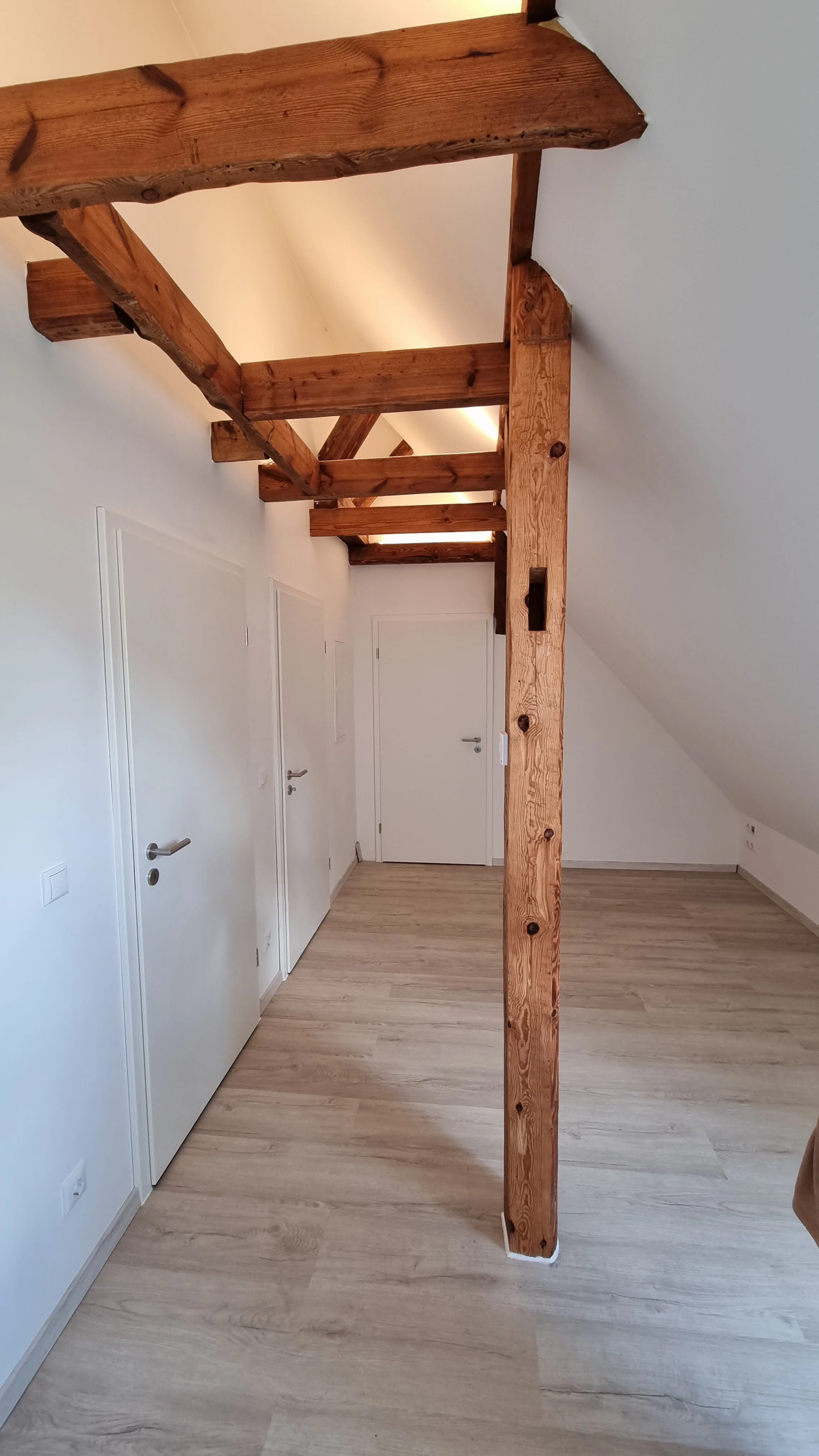 Innenraum mit weißen Wänden, Holzboden und sichtbaren Holzbalken an der Decke.