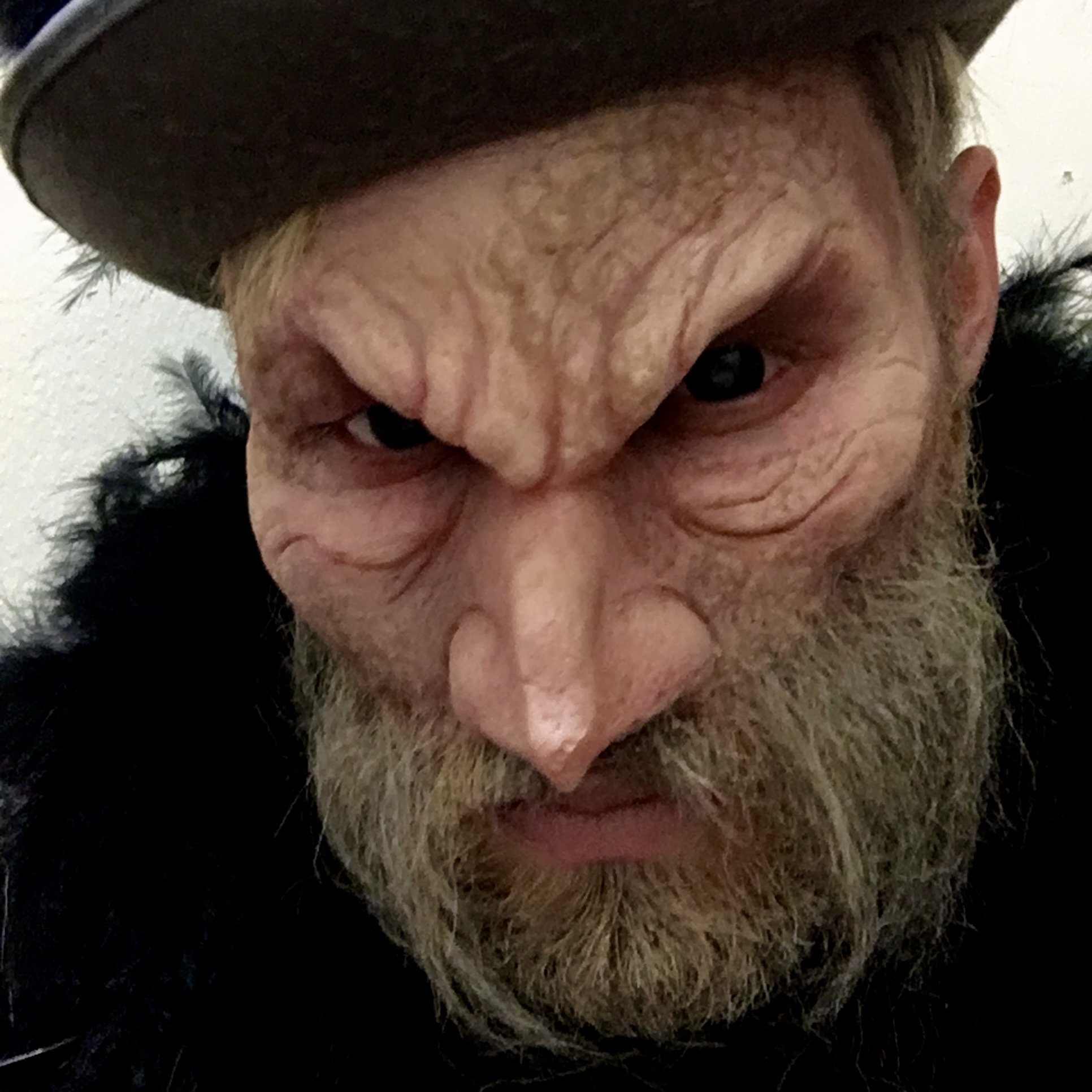 A person wearing a hat with a mean facial expression, scrunched face, and a beard.
