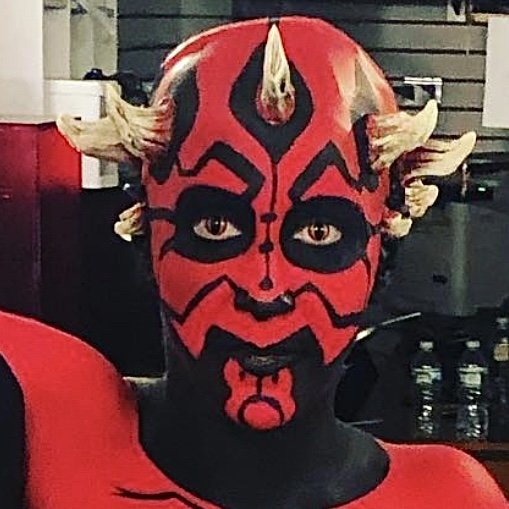 Person with red and black face paint resembling Darth Maul from Star Wars, with horns and face markings.