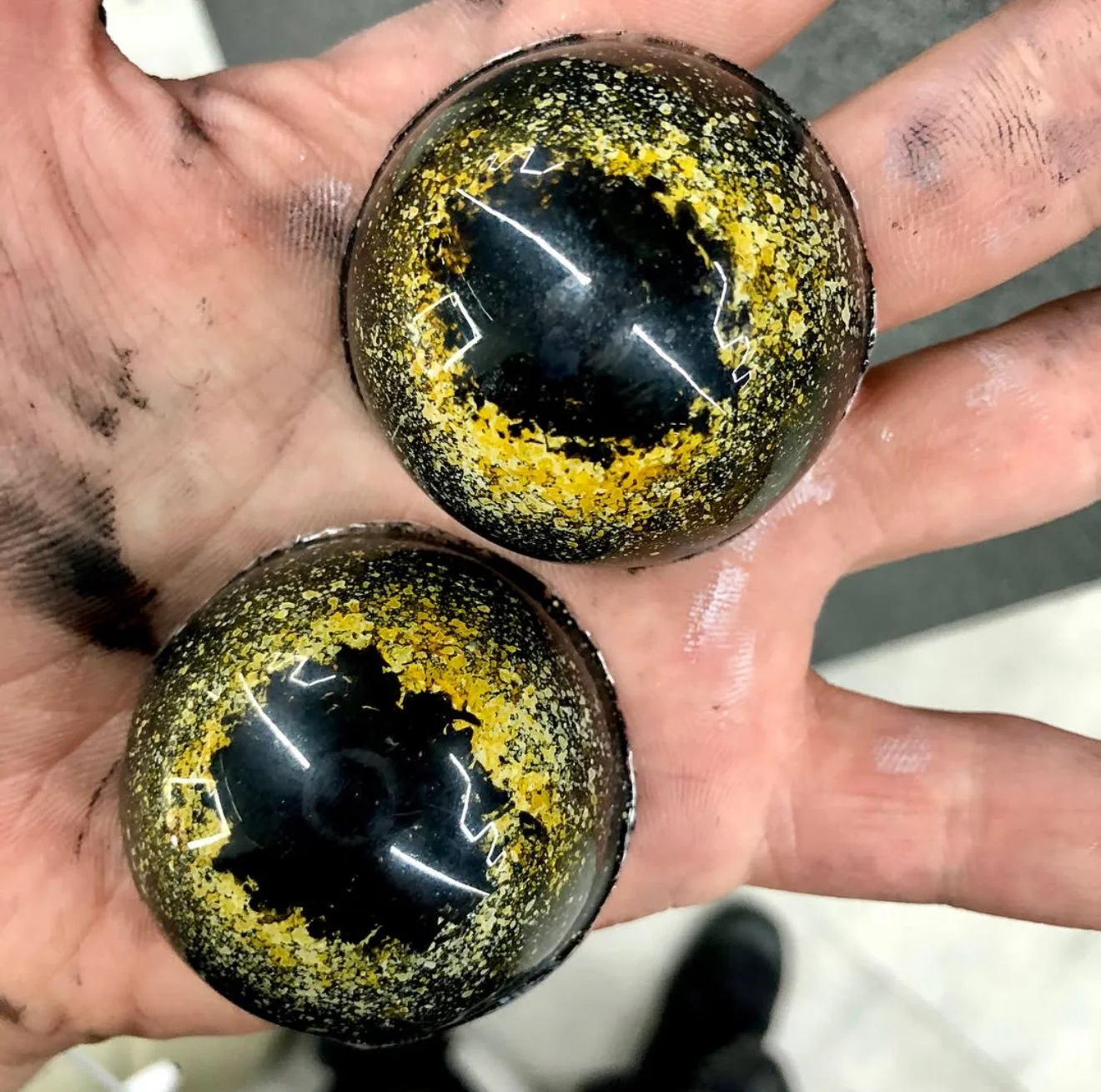 Two shiny black and yellow patterned glass marbles held in a person's hand.