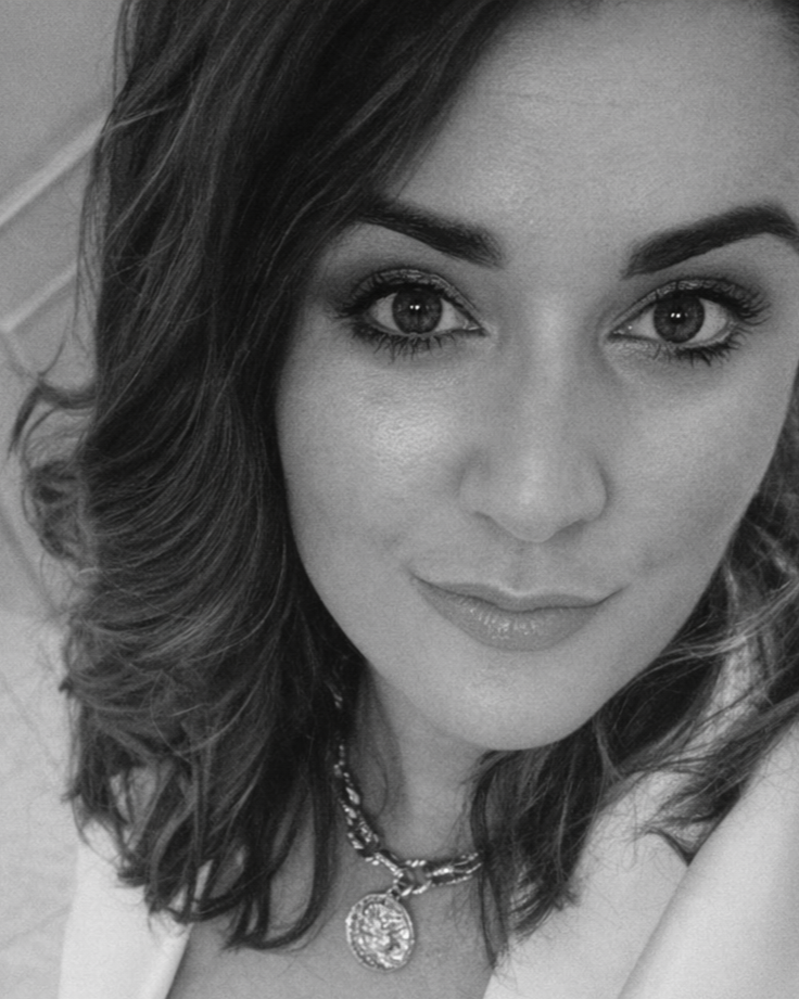 A woman with medium-length wavy hair, wearing makeup, a necklace, and a slight smile.