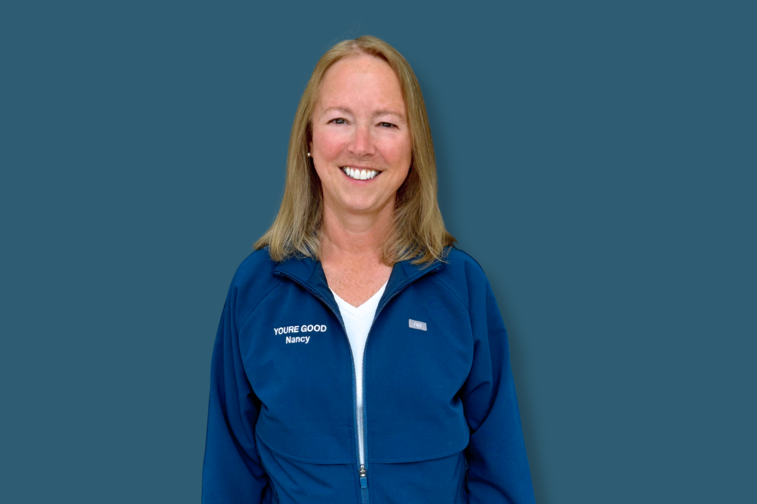A woman with blonde hair smiling, wearing a blue jacket with the words 'YOU'RE GOOD Nancy' on it, against a blue background.