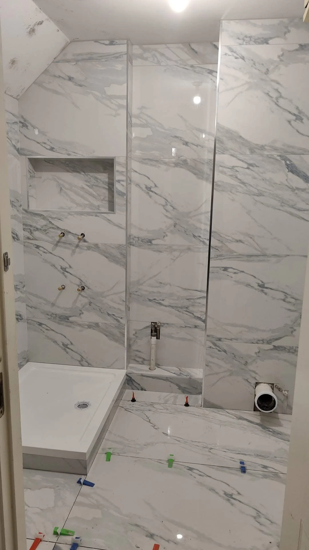 Bathroom under construction with marble tile walls and floor, a shower base installed, and plumbing fixtures visible