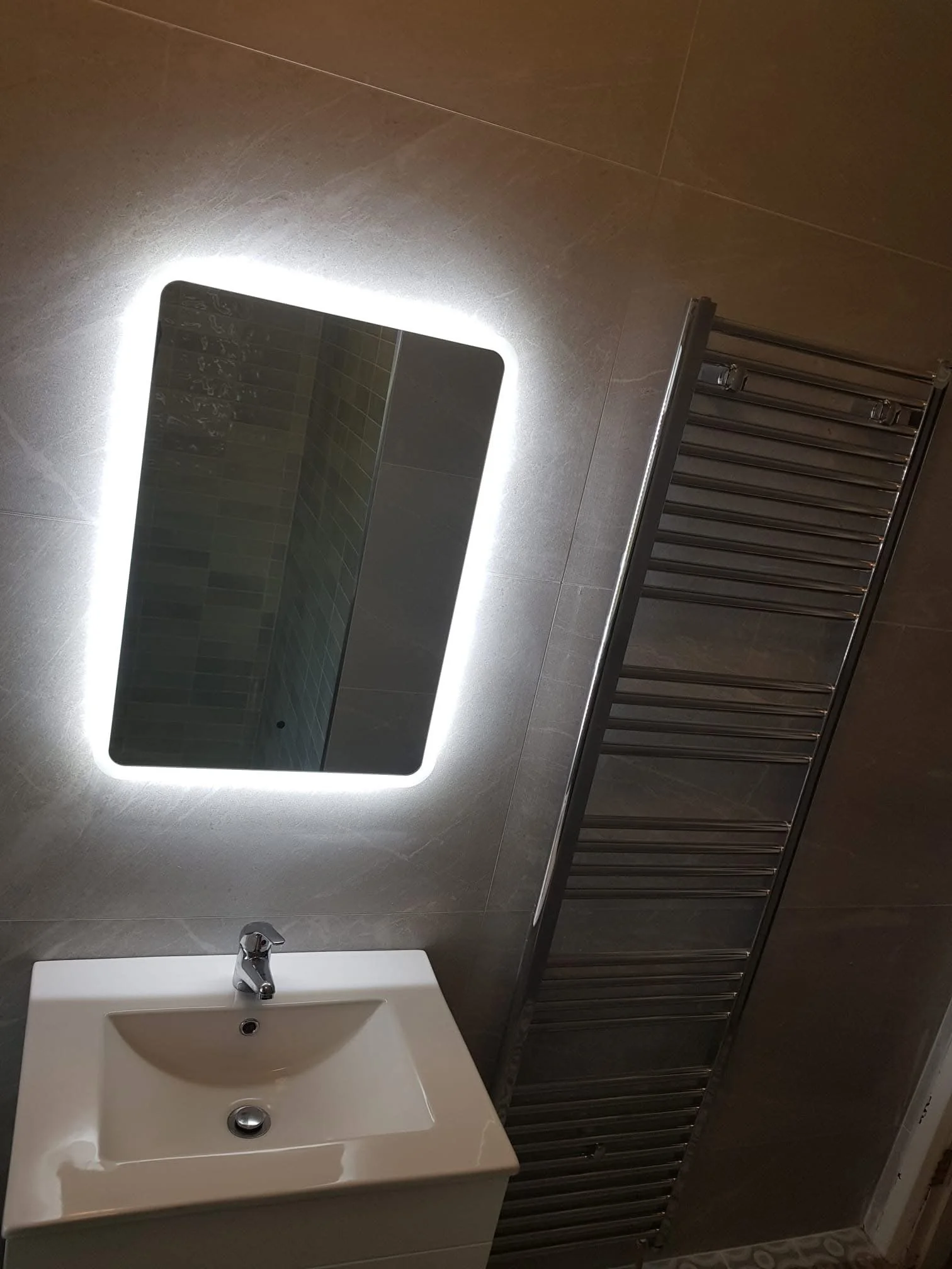 Bathroom with illuminated rectangular mirror above a white sink and a wall-mounted towel radiator.