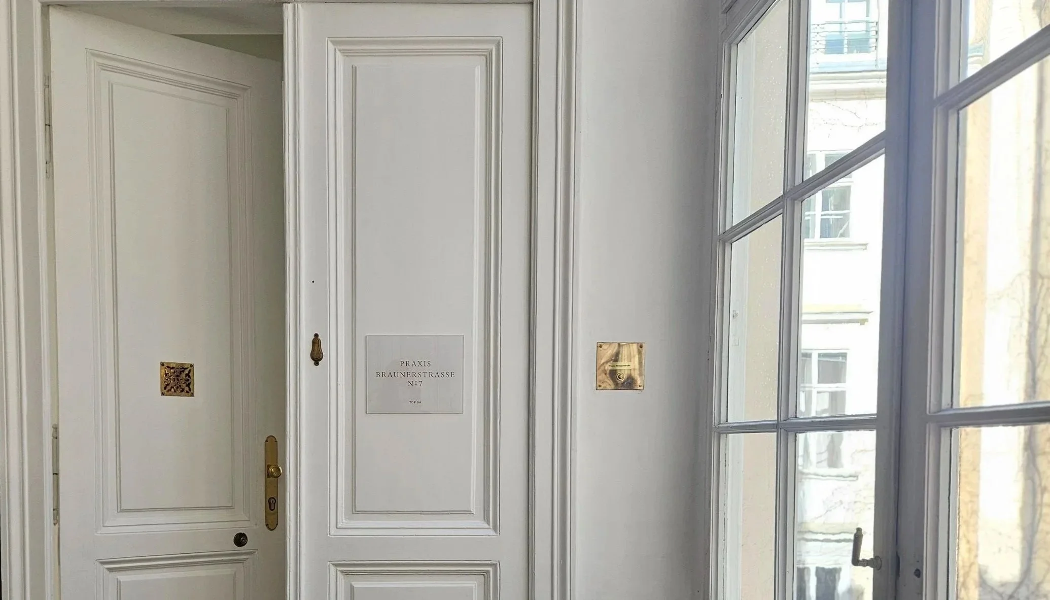 Alter Eingangstür mit einem Schild, das 'Praxis Braüenerstrasse Nr 7' beschreibt, neben einem Glasfenster.