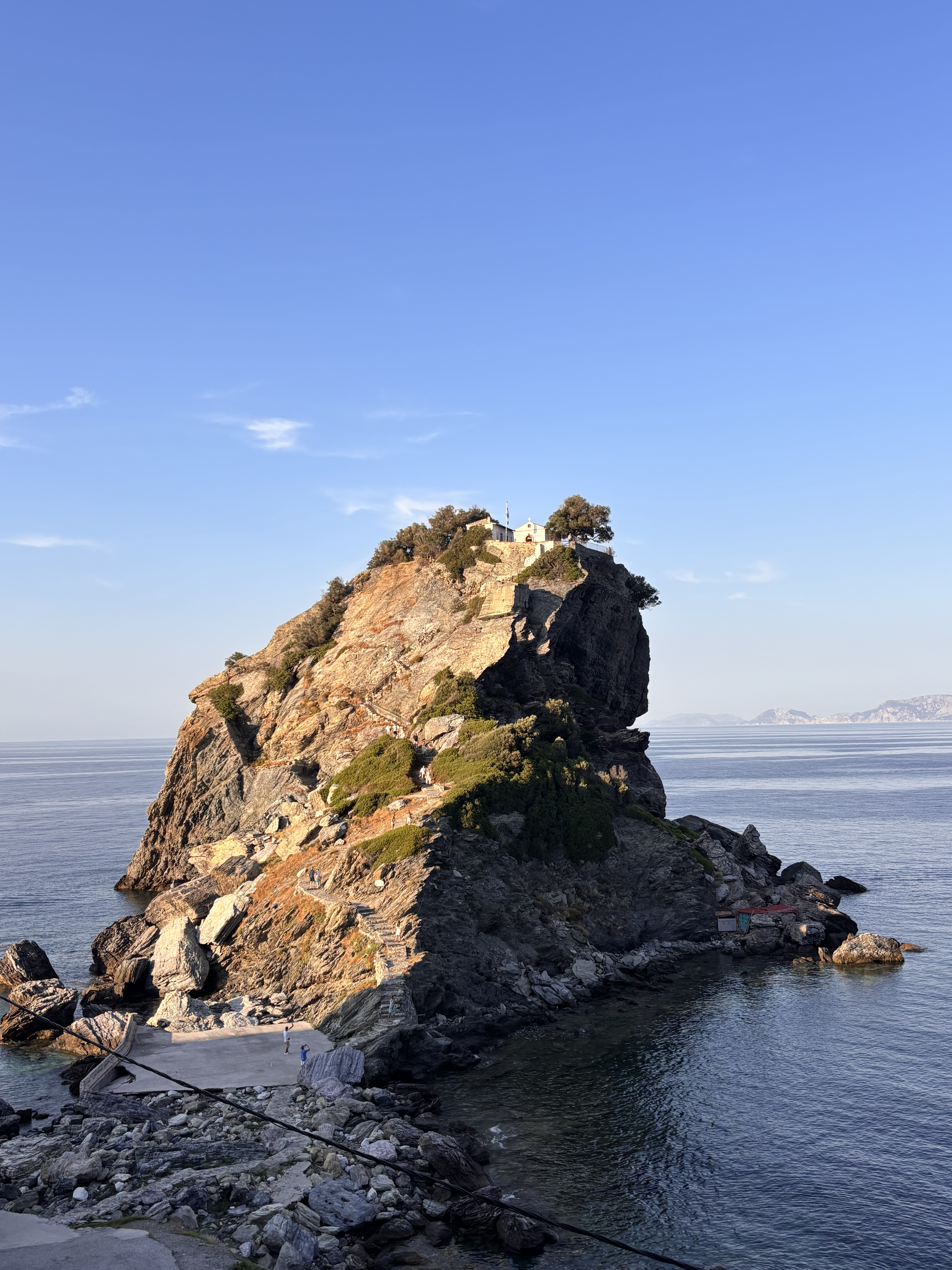A rocky cliff with a small white building on top, overlooking the ocean under a clear blue sky.