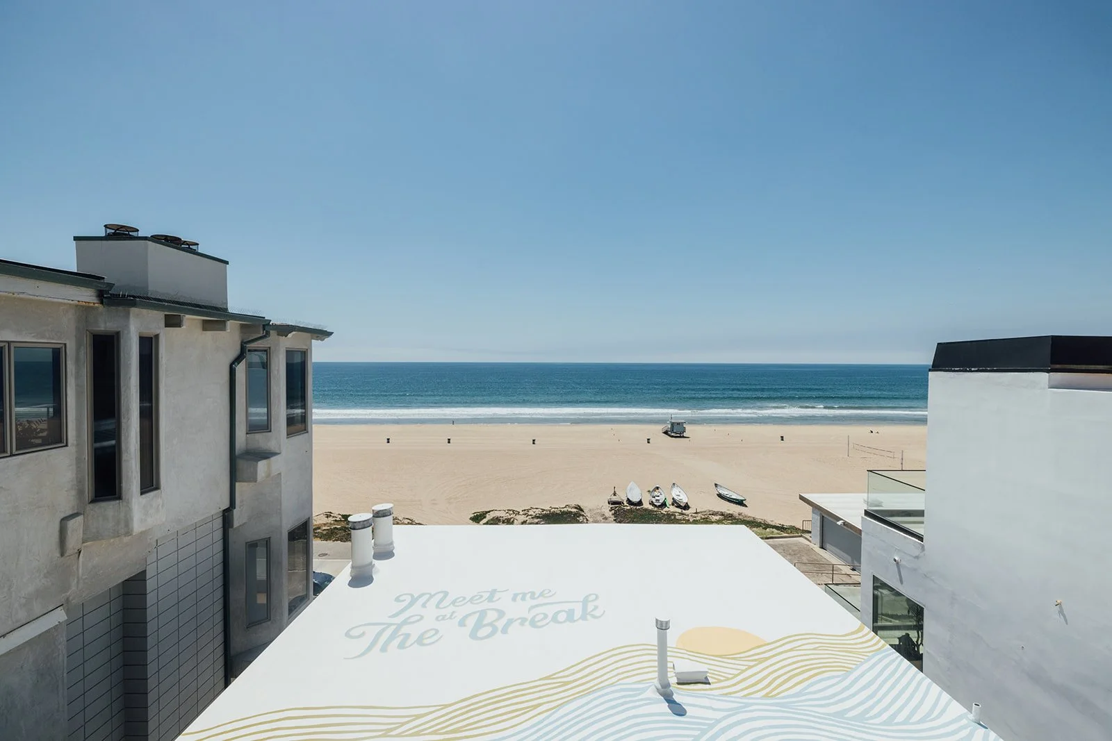 Ocean view from a balcony with sandy beach, boats, and clear blue sky