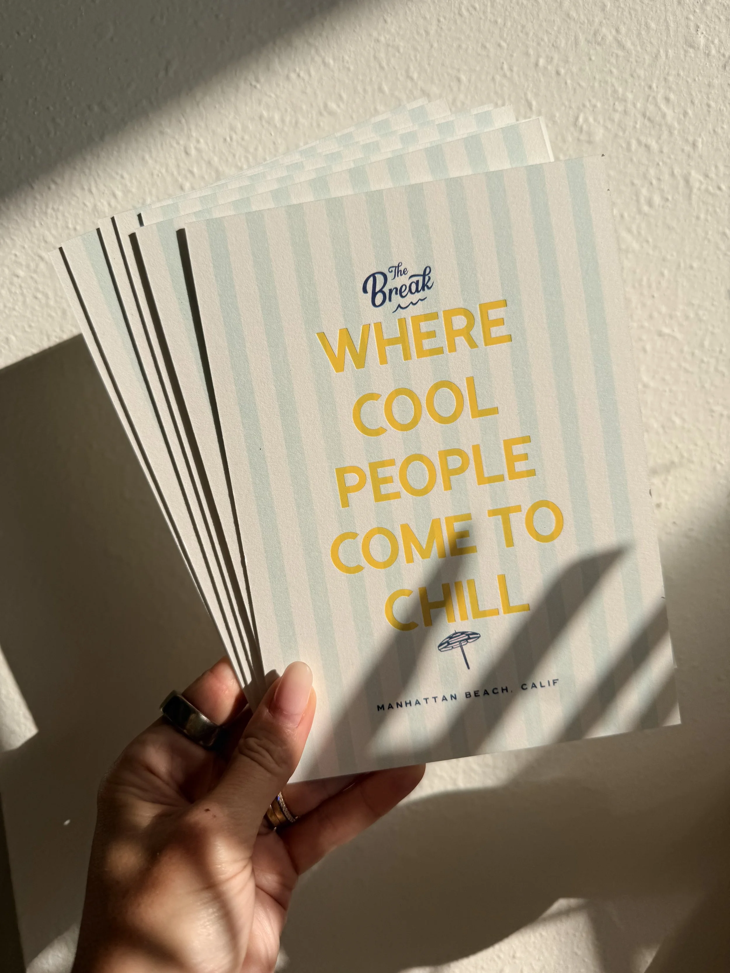 A hand holding a brochure titled "The Break: Where Cool People Come to Chill" against a textured wall, with a shadow cast on the wall.