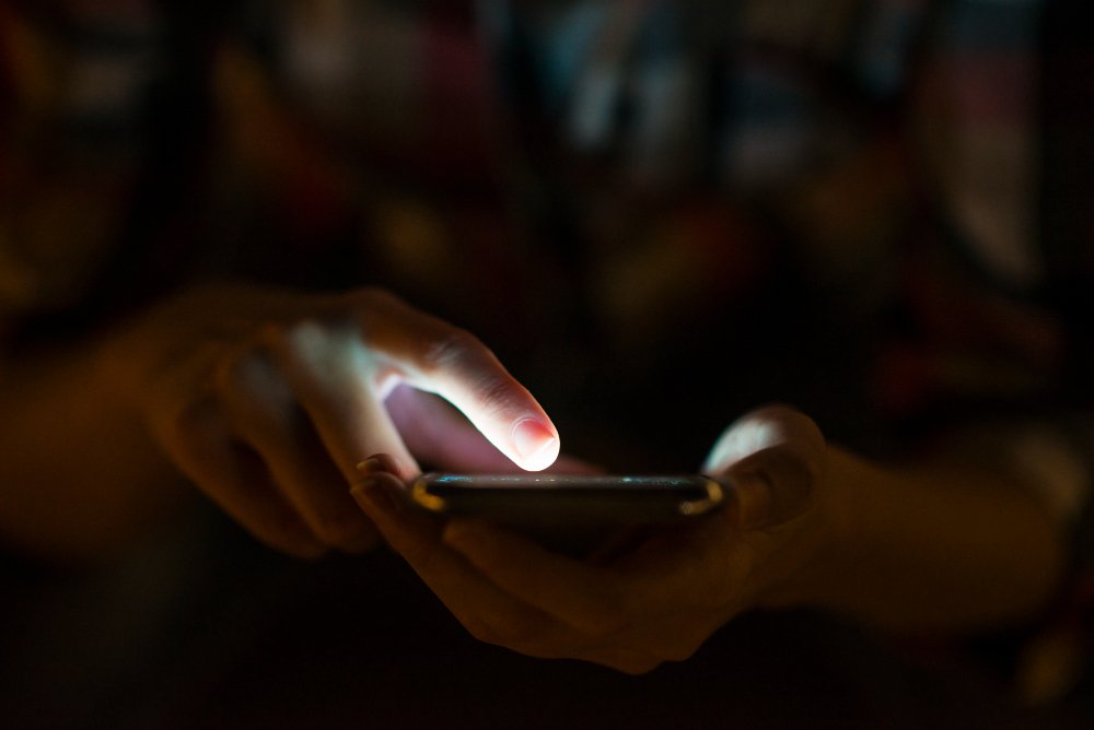 Person using a smartphone in a dark environment, with the screen illuminating their face.
