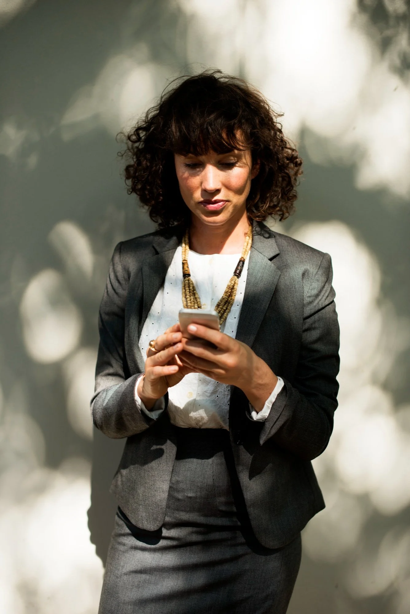 A woman in a gray business suit and white blouse looking at her phone.