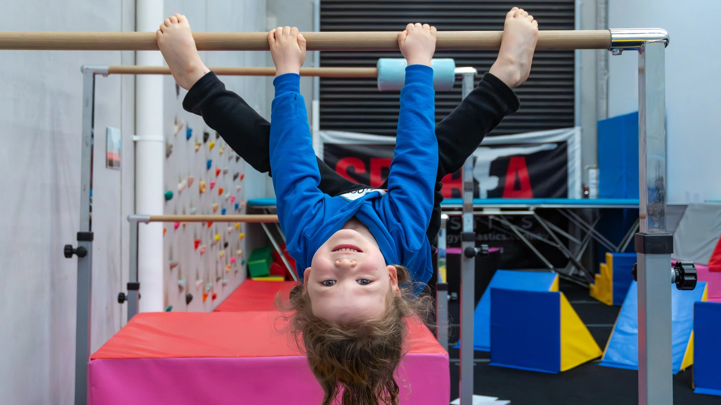 Child hanging upside down on a gymnastic bar in a gym facility.