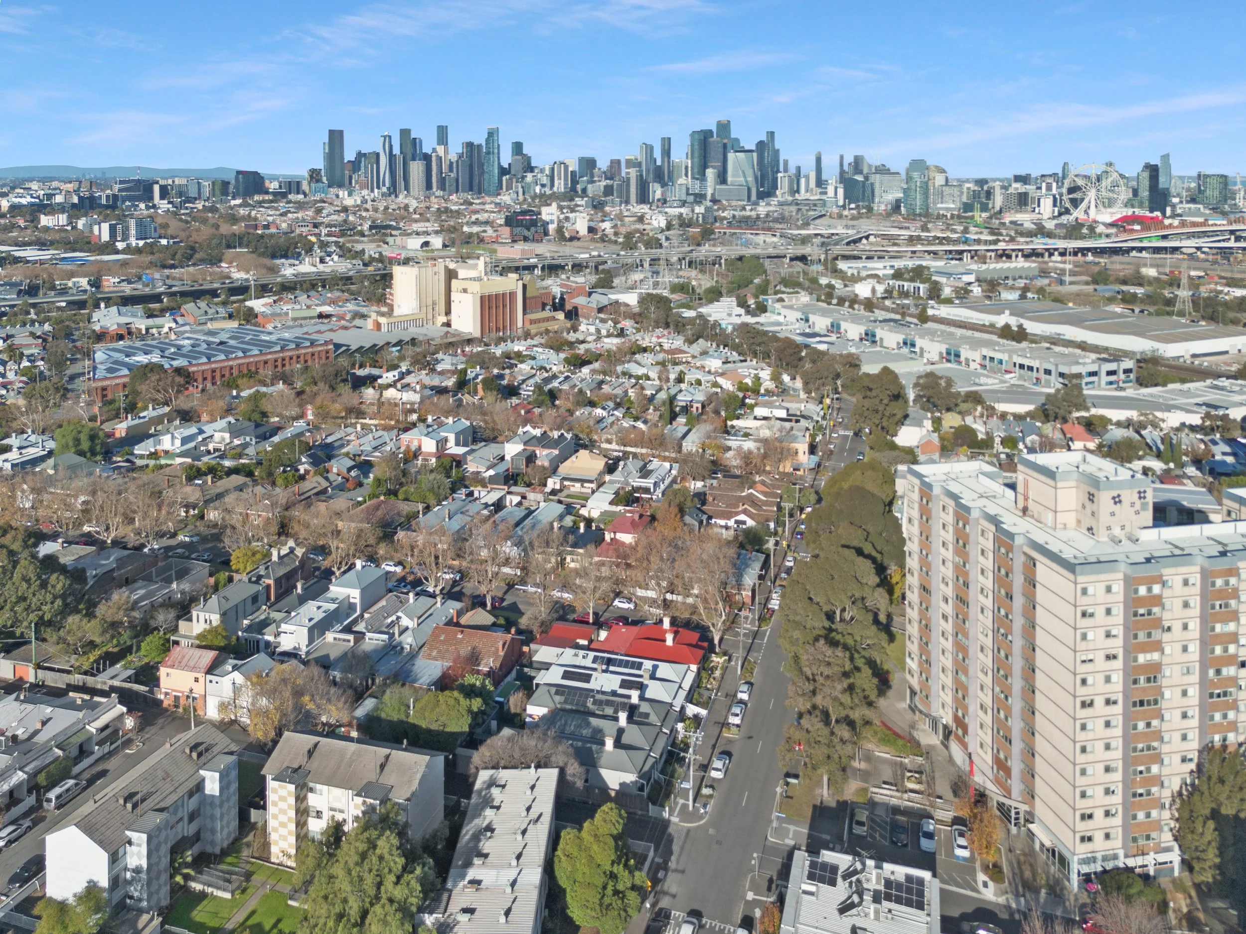 Aerial view of a city with a mix of residential and commercial buildings, including skyscrapers in the distance, a Ferris wheel, and a clear blue sky.