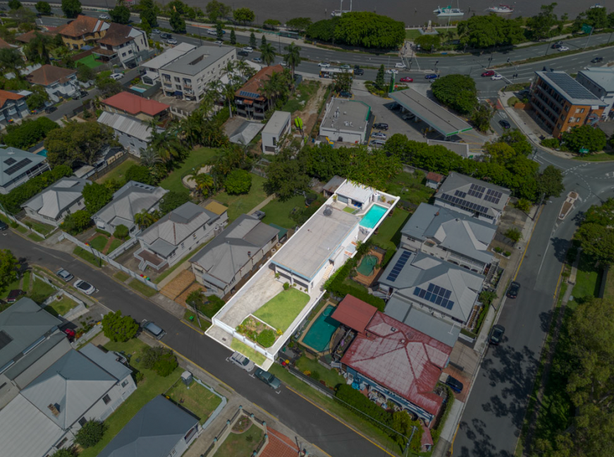Aerial view of a residential neighborhood with houses, trees, and a church with solar panels, near a busy highway. Includes a house with a swimming pool and backyard.