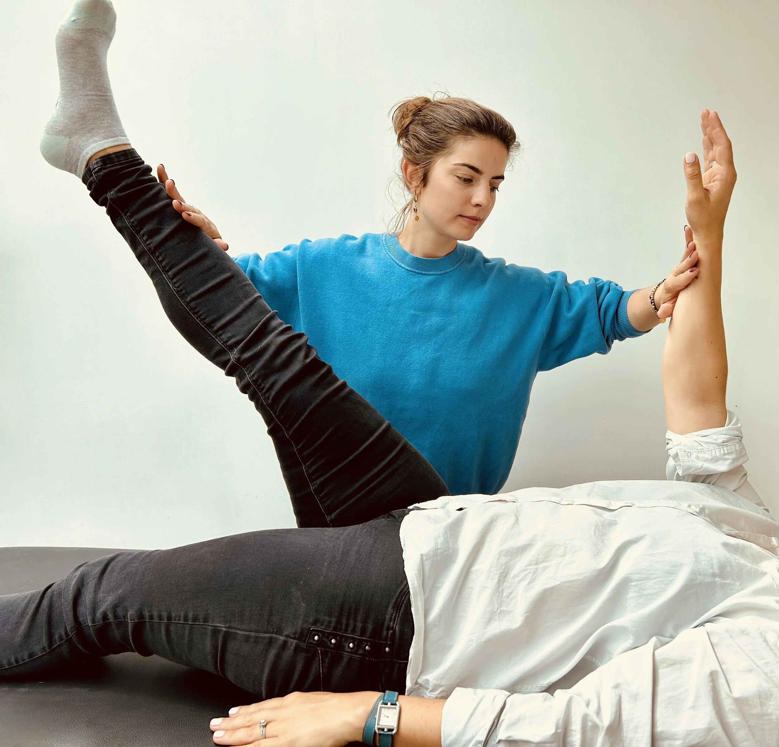 Une femme ajuste le bras d'une personne allongée pour une séance de thérapie ou de physiothérapie.