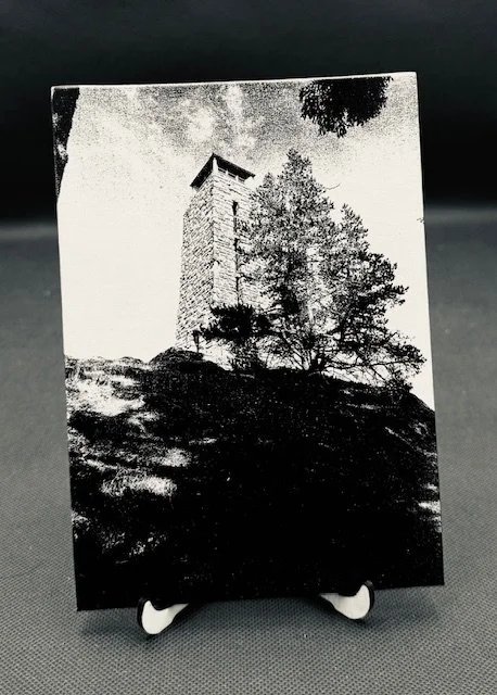 Black and white engraved photograph of a stone tower on a hill with trees around it.
