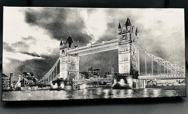 Black and white engraved photograph of Tower Bridge over the River Thames with a cloudy sky in the background.