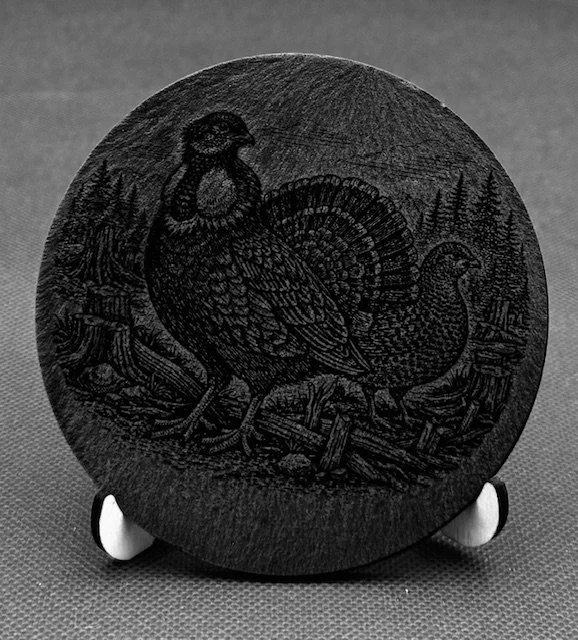 Engraved round stone featuring a turkey and a turkey hen in a natural setting with trees.