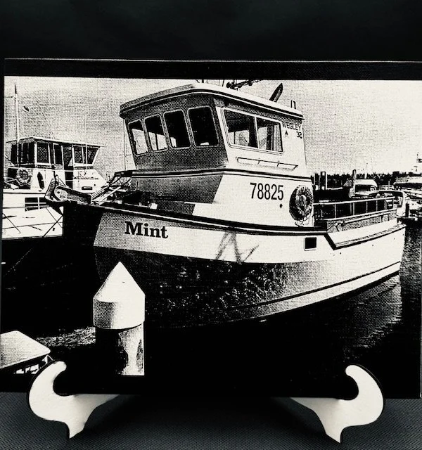 Black and white engraved photo of a boat named 'Mint' docked at a marina, with other boats and water in the background.