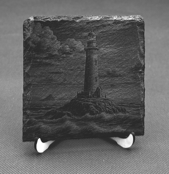Black and white painting of a lighthouse on a rocky island, with stormy clouds in the background, displayed on a small easel.