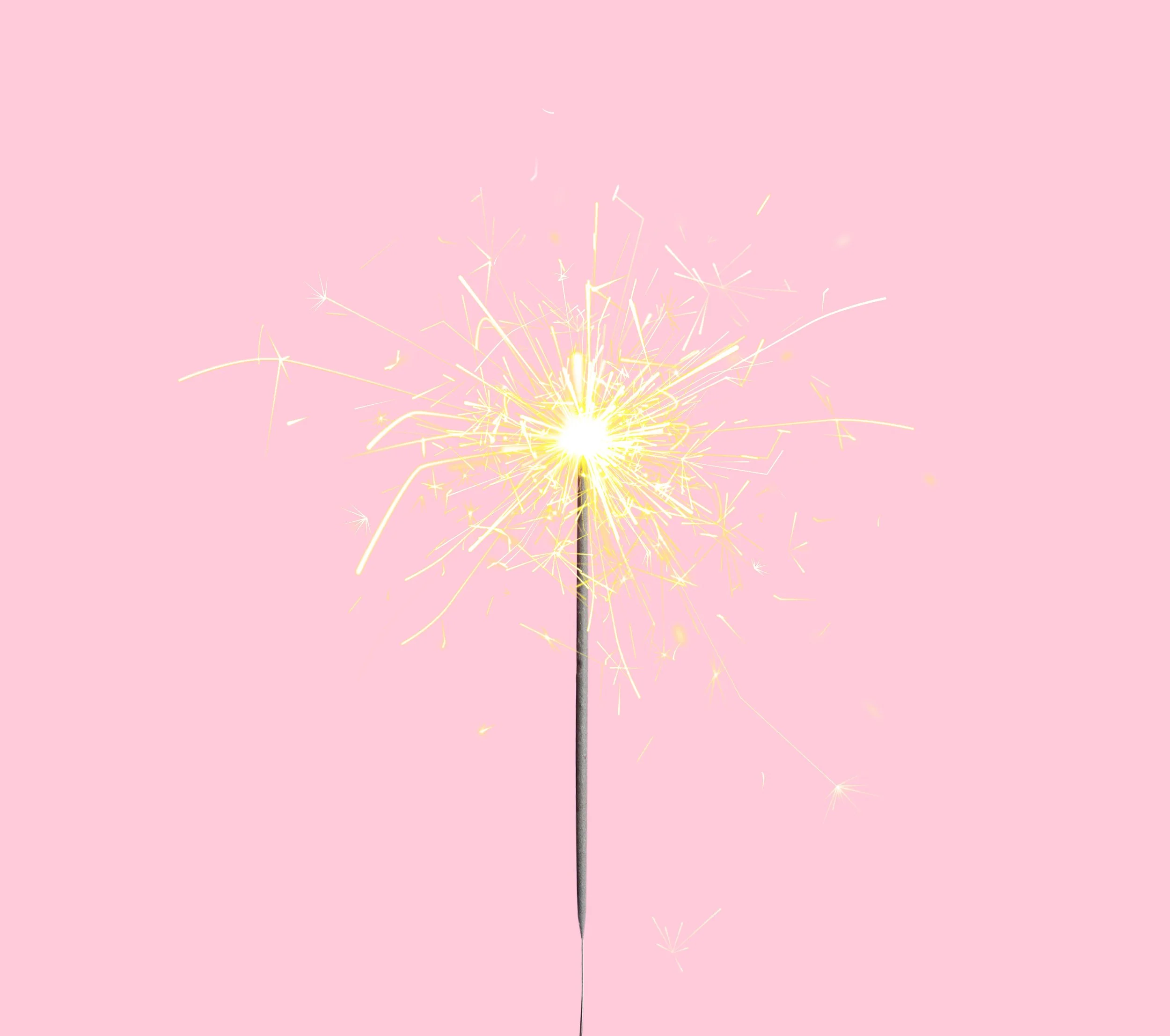 Pink background with a lit sparkler emitting bright yellow sparks.