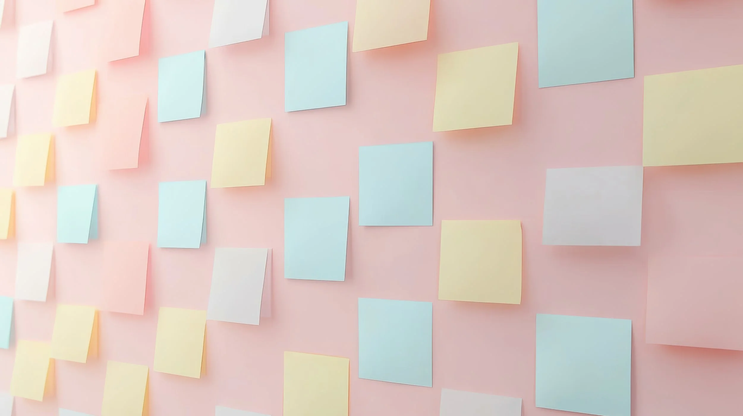 A pink wall covered with multiple pastel-colored sticky notes in shades of yellow, blue, and white, arranged in a grid-like pattern.